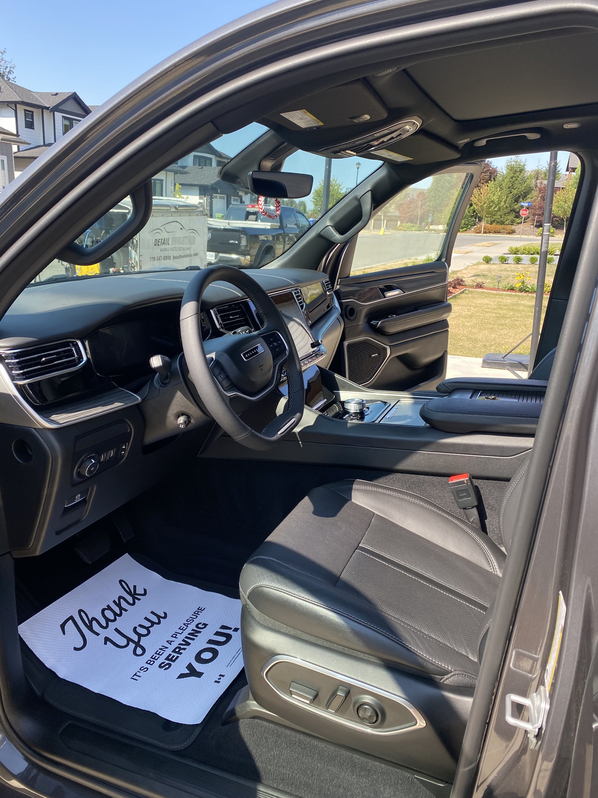 The interior of a modern vehicle with a black dashboard, steering wheel, center console, and black leather seat, with a printed thank you note on the floor reading 'Thank You. It's been a pleasure serving you!'