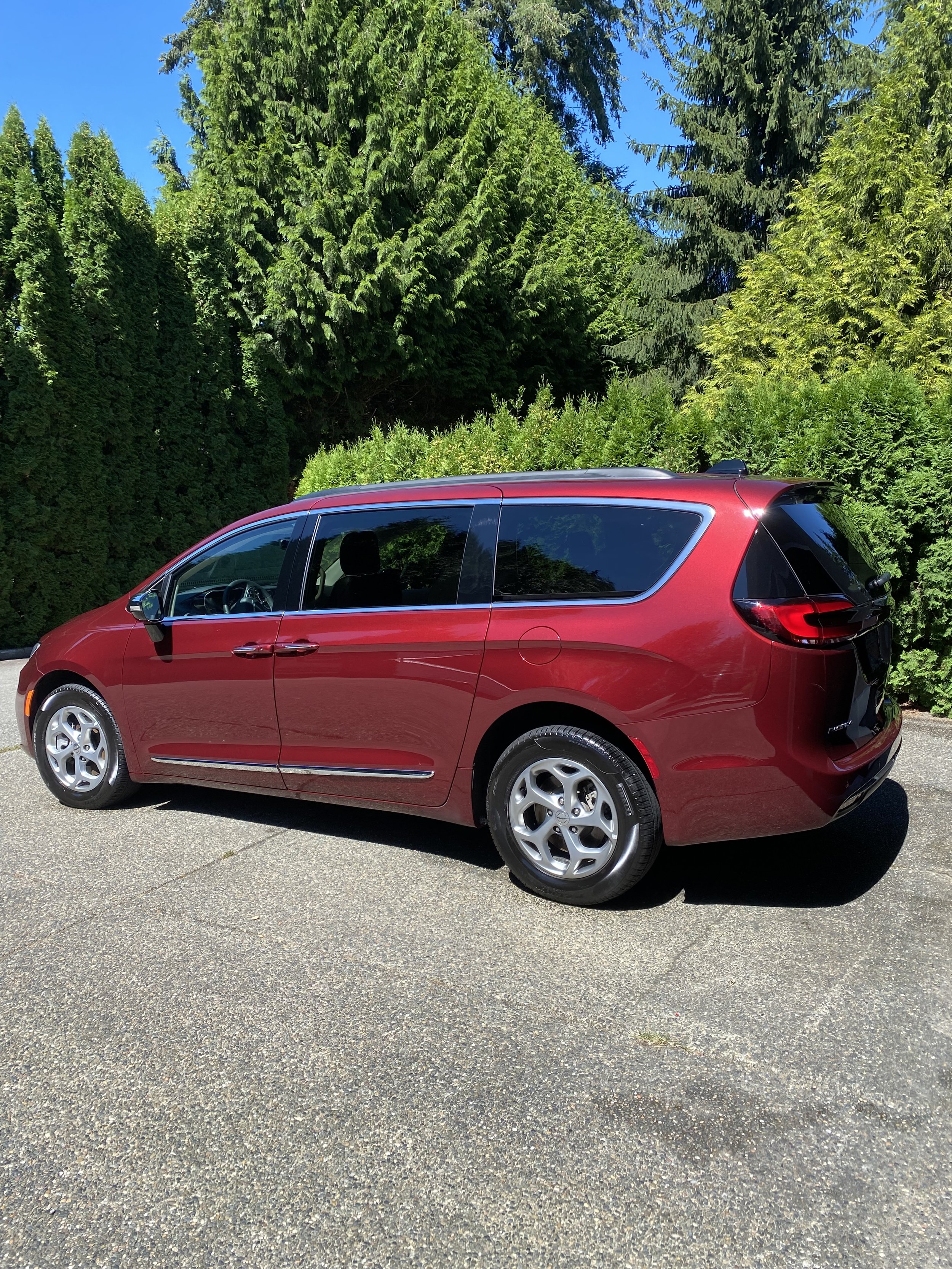 A red minivan parked on a driveway with green trees and bushes in the background.