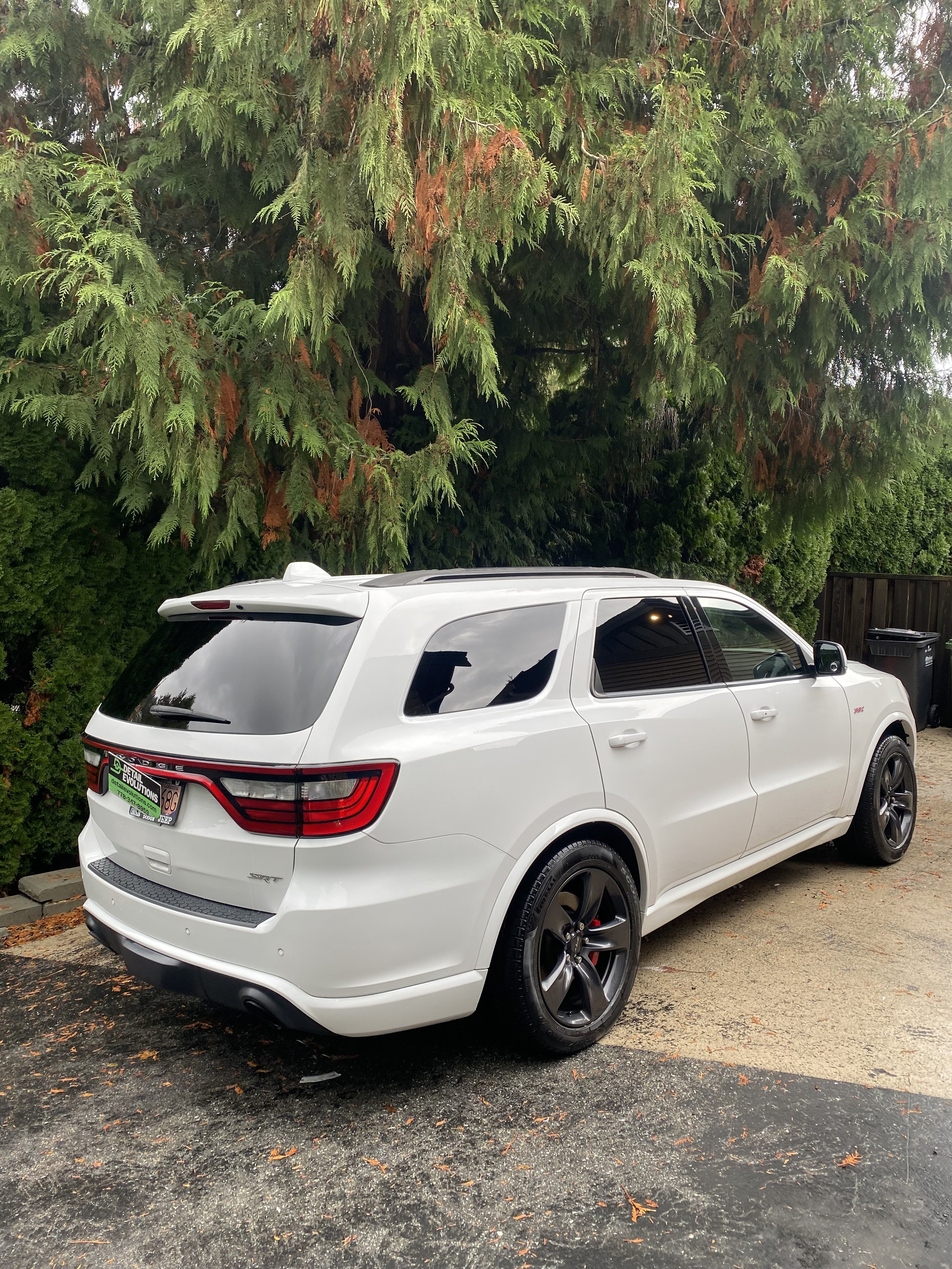 White SUV parked on a driveway with green trees in the background.